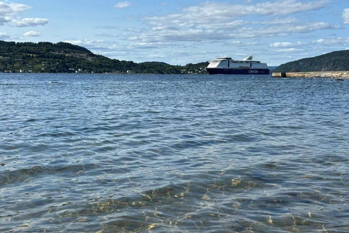 Un ferry de croisière de Color Line sur le fjord d’Oslo, vu depuis une rive à l’eau claire et peu profonde, entre des collines boisées