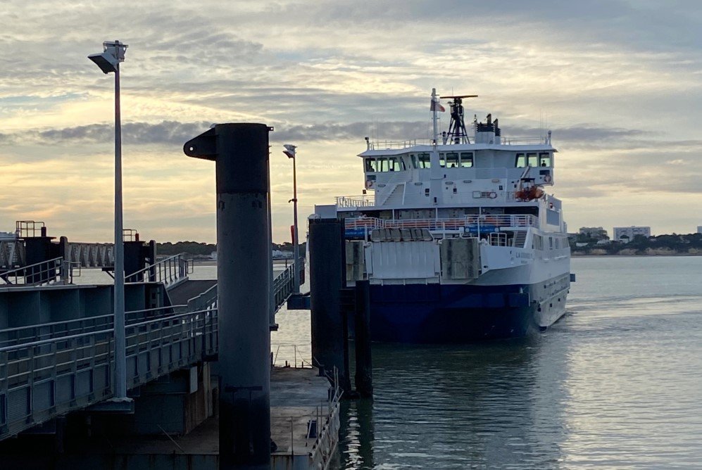 La Gironde arrive vers l’embarcadère dans une lumière rasante, avec à gauche au premier plan une bitte d’amarrage en acier et une passerelle