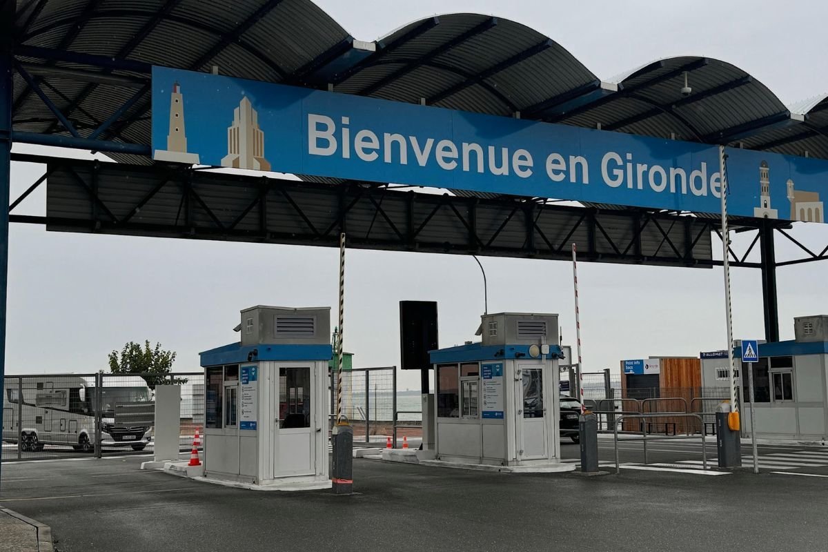 Deux petites guérites avec barrières sous un auvent portant le panneau Bienvenue en Gironde, avec un camping-car dans la file à gauche