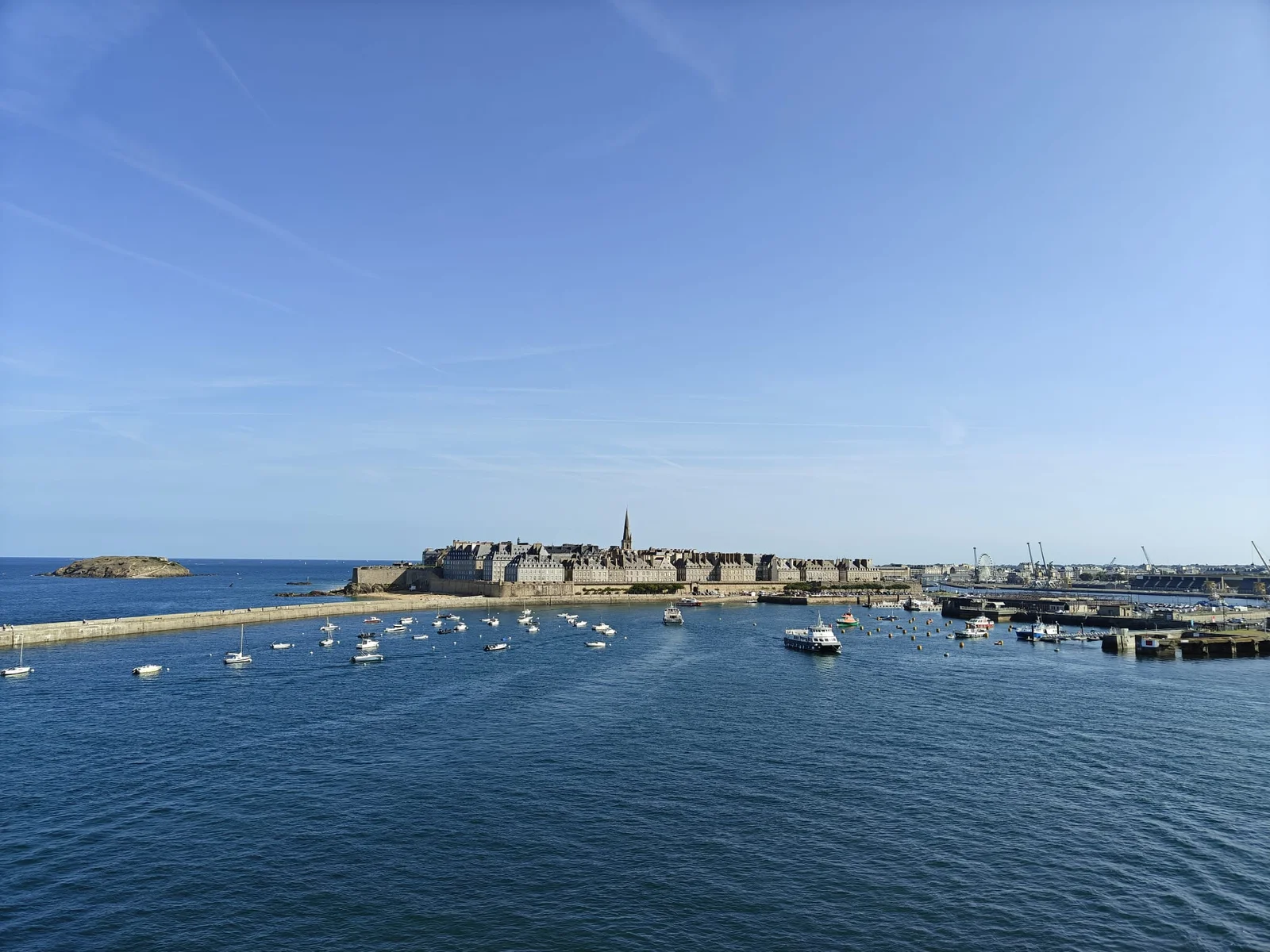 La ville fortifiée de Saint-Malo et le clocher de la cathédrale, vus depuis le pont du ferry qui s’éloigne, avec des dizaines de bateaux sur l’eau
